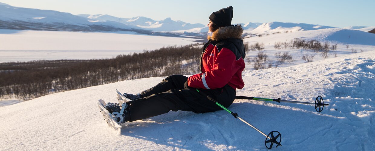 A woman on snowshoes gazes out across a vast frozen landscape in Kilpisjarvi